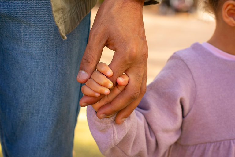 Imagem em close na mão de um adulto segurando a mão de uma criança