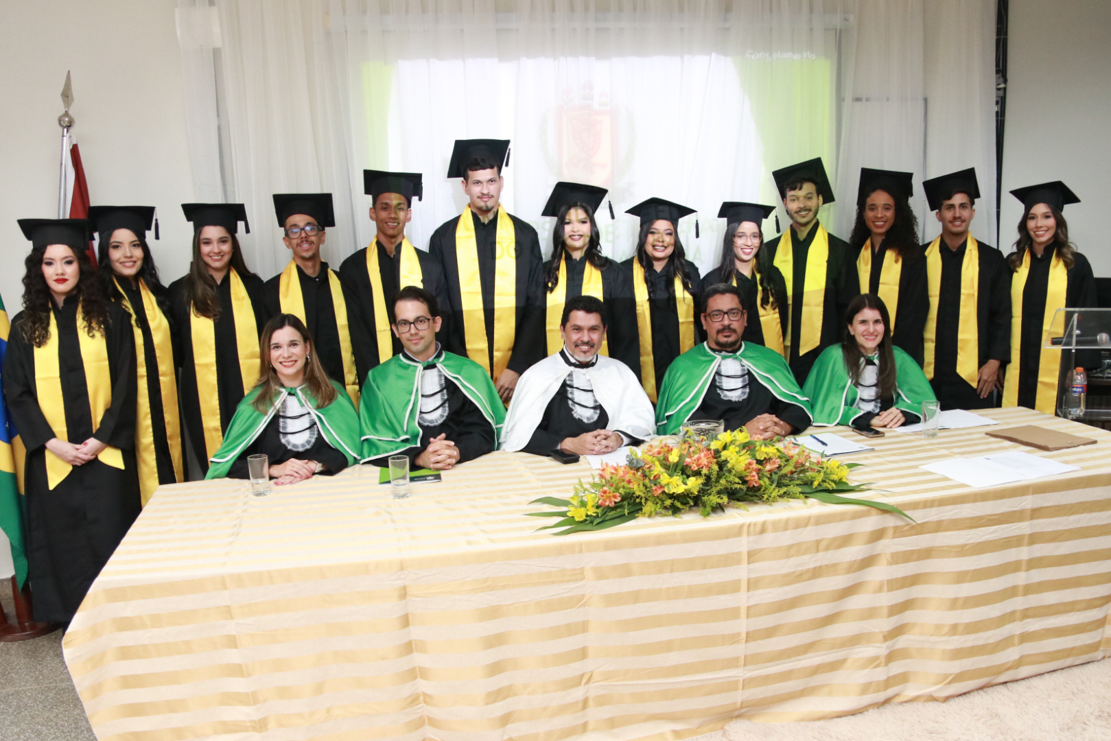 Imagem de formandos e mesa durante colação de grau do Curso de Farmácia da UFOB
