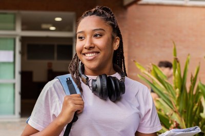 Estudante com mochila e fone de ouvindo chegando a Universidade