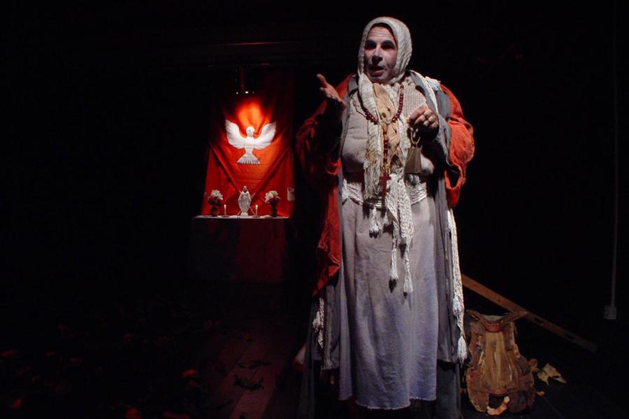 Imagem do ator Graça Veloso vestido com uma túnica com fundo escurecido e um alto do Divino Espírito Santo