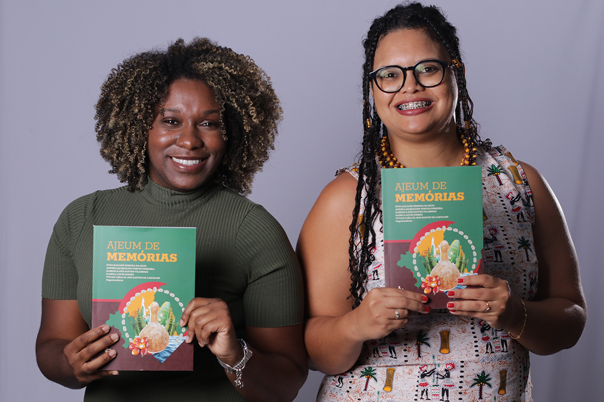 Imagem das professoras Etna Kaliane Pereira da Silva e Izabela Gomes segurando o livro “Ajeum de Memórias”, que será lançado nesta quinta (9), em Barreiras