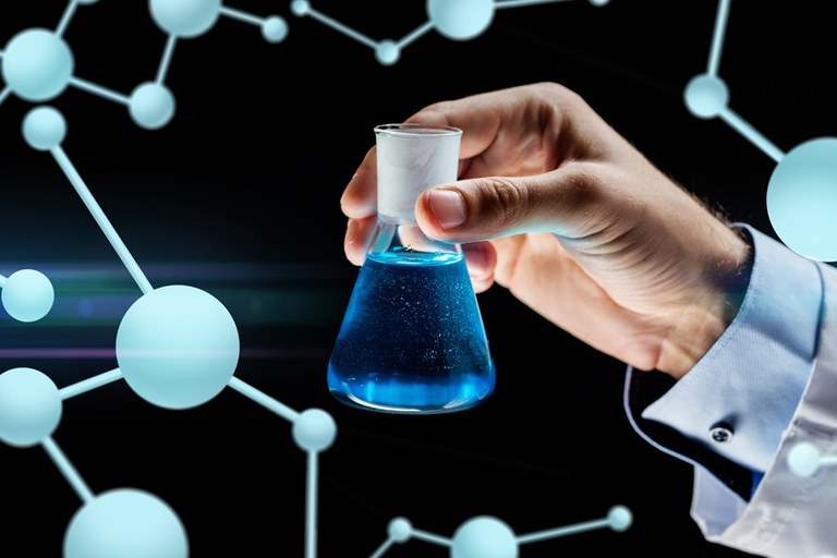 Imagem em fundo preto com mão segurando recipiente com líquido azul e fundo