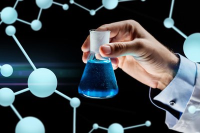 Imagem em fundo preto com mão segurando recipiente com líquido azul e fundo