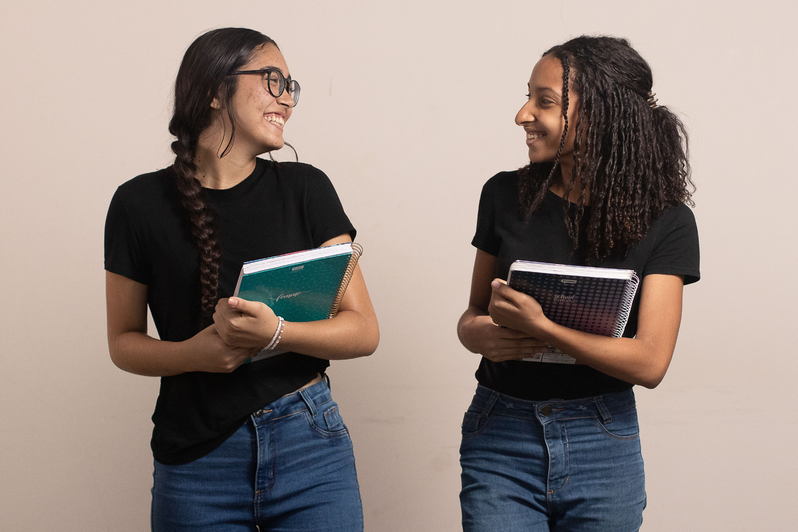 Foto de duas estudantes com caderno na mão e sorrindo uma para a outra