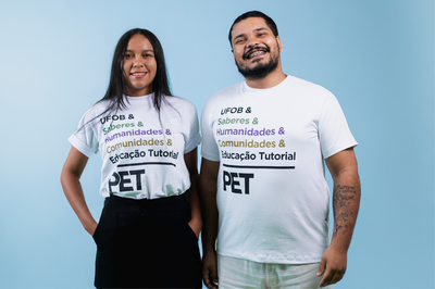Dois jovens estudantes da UFOB. Uma mulher à esquerda e um homem à direita. Ambos vestem camisetas iguais, na cor branca, estampadas com a marca do Programa de Educação Tutorial - PET