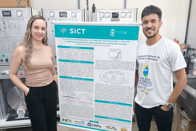 Imagem de duas pessoas em frente ao banner do Seminário de Iniciação Científica e Tecnológica da UFOB