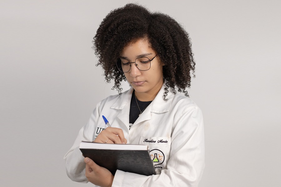 Foto de estudantes da UFOB com jaleco e escrevendo num caderno