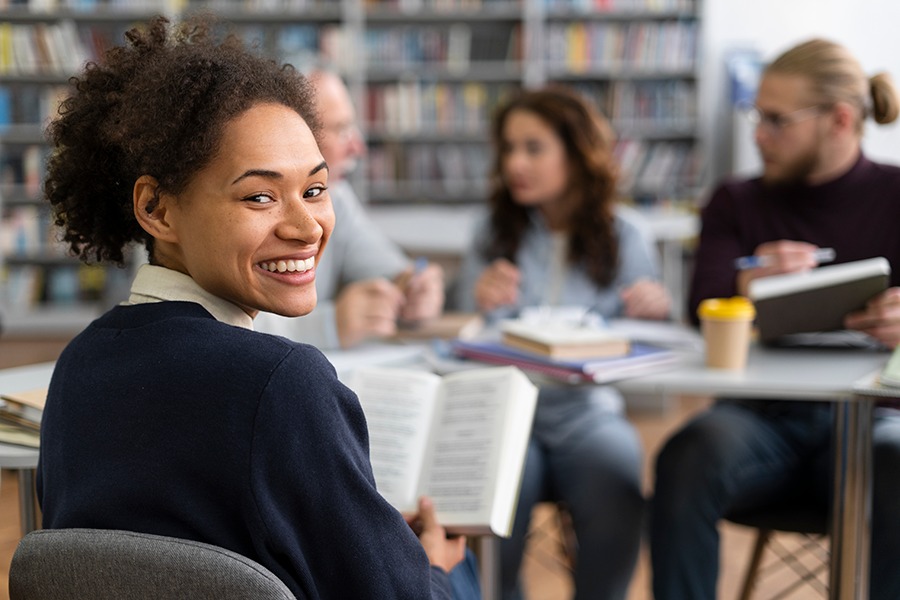 Imagem de estudantes numa biblioteca com mulher lendo em primeiro plano