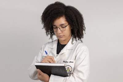 Estudante da UFOB com jaleco e fazendo anotações no caderno